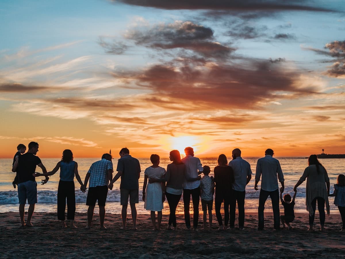 A family holding hands on the shore at sunset, silhouetted against a golden sky
